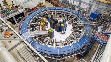 The Muon g-2 ring sits in its detector hall amidst electronics racks, the muon beam-line, and other equipment
