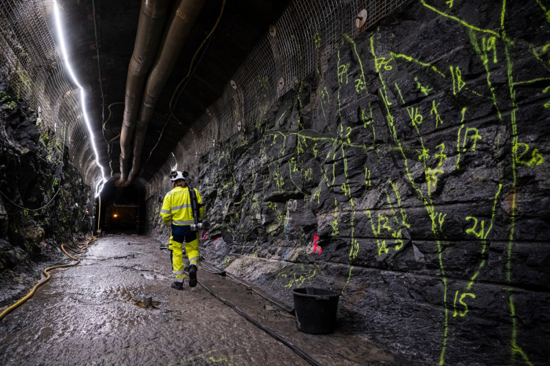 zidul cu marcații geologice a unui tunel de depozitare a deșeurilor nucleare și un bărbat în costum de protecție care merge pe lângă