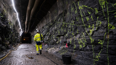 zidul cu marcații geologice a unui tunel de depozitare a deșeurilor nucleare și un bărbat în costum de protecție care merge pe lângă