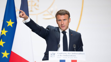 Emmanuel Macron la pupitrul prezidențial cu mâna ridicată și degetul arătător