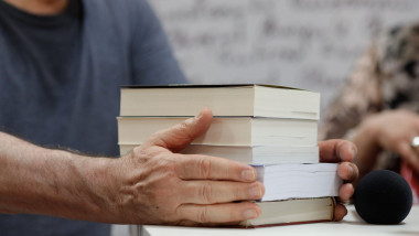 Shallow depth of field (selective focus) details with the hands of a man on a pile of books during a book release event.