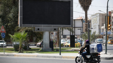 Panou publicitar închis în Bagdad în timp ce un motociclist merge pe drum