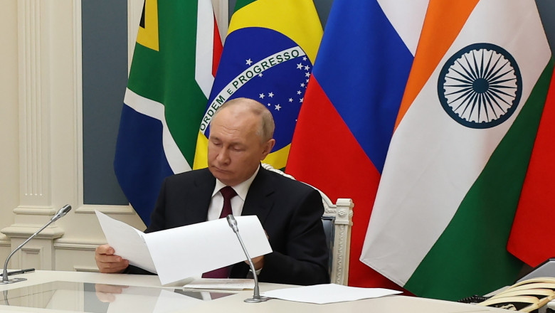 Putin cu steaguri ale țărilor BRICS în spate citește de pe o foaie de hârtie