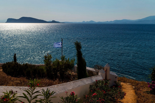 Hydra, Greece. 24th July, 2020. A Greek flag is waving in the wind. The island of Hydra, which covers almost 50 square kilometres, is 65 kilometres south-west of Athens. Cars, neon signs and plastic chairs are prohibited on the island. Credit: Angelos Tzo
