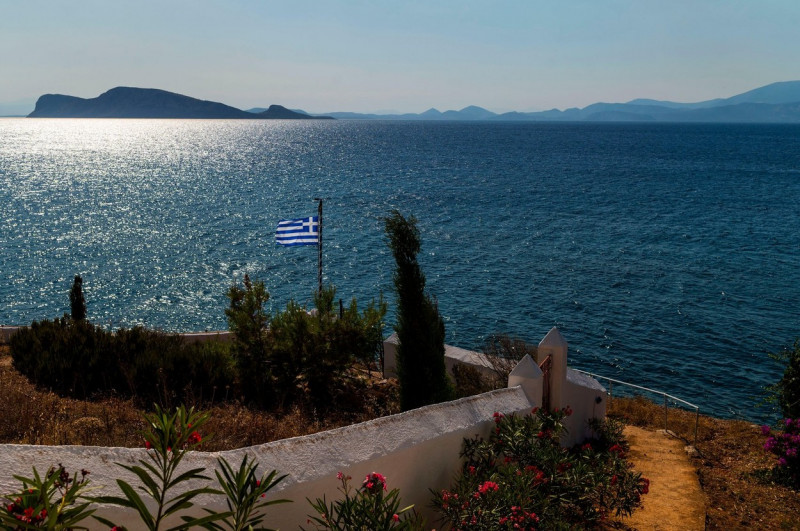 Hydra, Greece. 24th July, 2020. A Greek flag is waving in the wind. The island of Hydra, which covers almost 50 square kilometres, is 65 kilometres south-west of Athens. Cars, neon signs and plastic chairs are prohibited on the island. Credit: Angelos Tzo