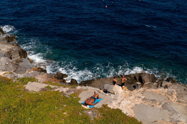 Hydra, Greece. 24th July, 2020. People bask in the sun by the water. The island of Hydra, which covers almost 50 square kilometres, is 65 kilometres south-west of Athens. Cars, neon signs and plastic chairs are prohibited on the island. Credit: Angelos Tz