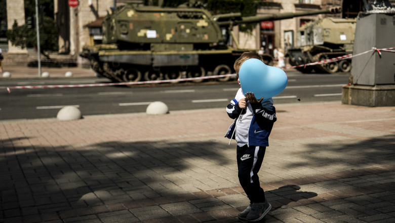 copil pe stradă cu un balon în mână și un tanc rusesc în fundal