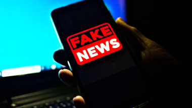 Hand holding a cell phone where the words fake news are shown on the screen. low-light, dramatic image suggesting danger or a dangerous attitude.