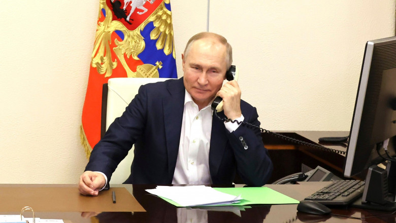 Putin vorbește la telefon cu fir, în timp ce stă la biroul de la Kremlin, cu steagul Rusiei în spate