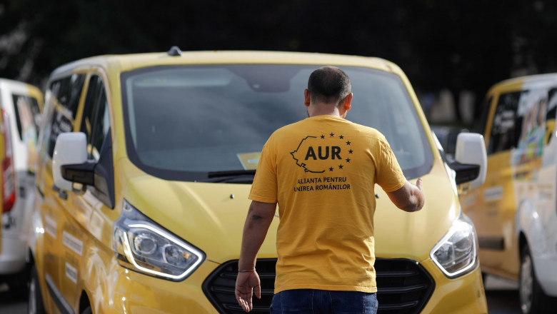 membru AUR cu trocol galben cu logo-ul partidului cu spatele, in fata unei masini galbene