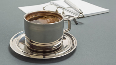 cana de cafea pe un birou in fata unui caiet si a unei perechi de ochelari