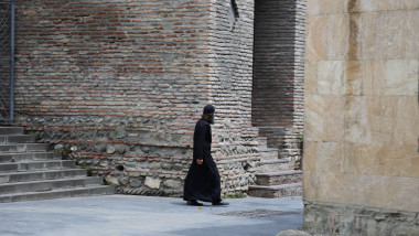 calugar ortodox merge pe langa zidulunei biserici