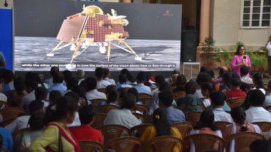 oameni urmăresc pe un ecran informații despre misiunea lunară a Indiei