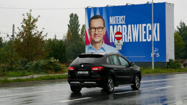 mașina pe stradă în mers și un panou electoral cu premierul Poloniei