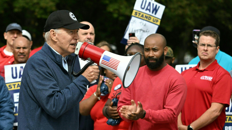 Joe Biden cu un megafon blazonat cu steagul SUA, printre oameni îmbrăcați în roșu și cu pancarte în mâini