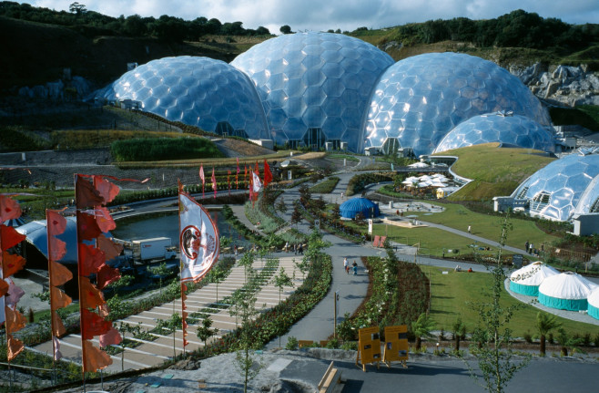 Eden Project. General view over the Humid tropics Biome exterior with line of coloured flags and visitors on path to entrance.