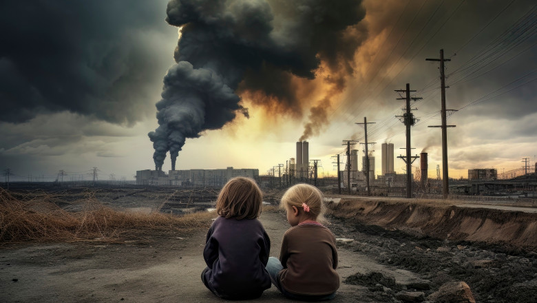 Doi fetițe care privesc spre fabrici care emit gaze și fum în atmosferă