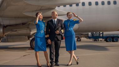 Un pilot și două însoțitoare de bord pozează lângă un avion