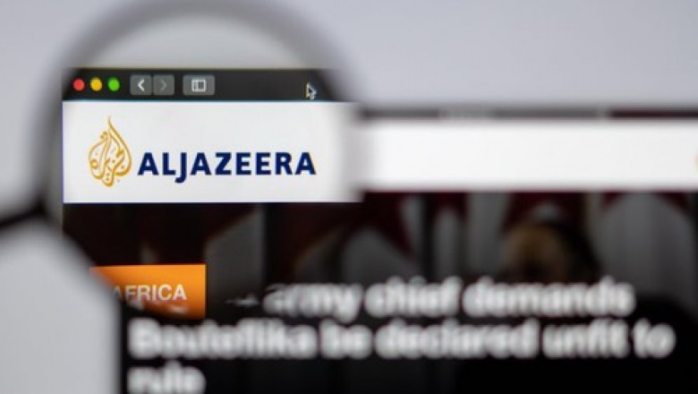 Arabian News media Al Jazeera website homepage. Al Jazeera logo visible through a magnifying glass.