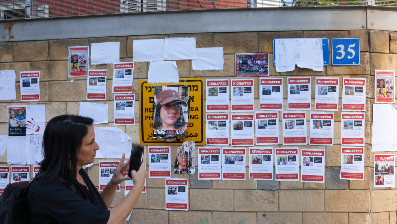 O femeie în negru face o poză cu telefonul zidului pe care sunt puse afișele cu ostaticii luați de Hamas în Gaza
