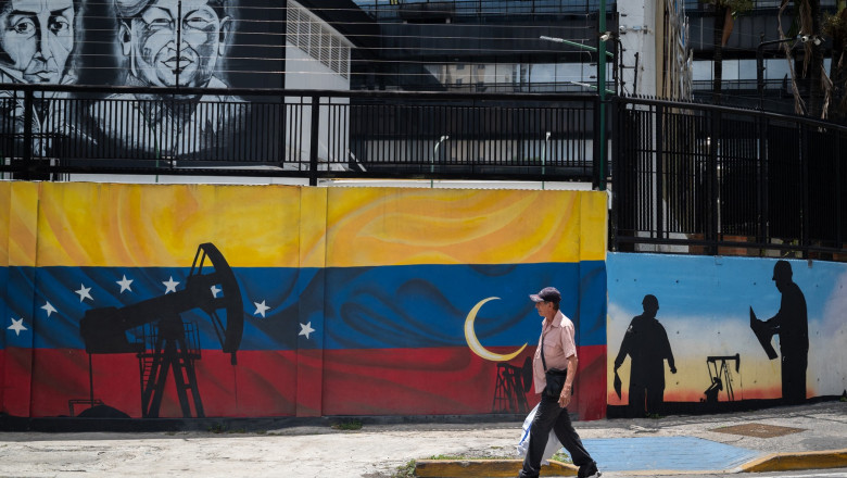 Un bărbat trece pe lângă o pictură murală cu steagul Venezuelei pictat pe un perete din fața sediului PDVSA (Petroleros de Venezuela, SA) din Caracas