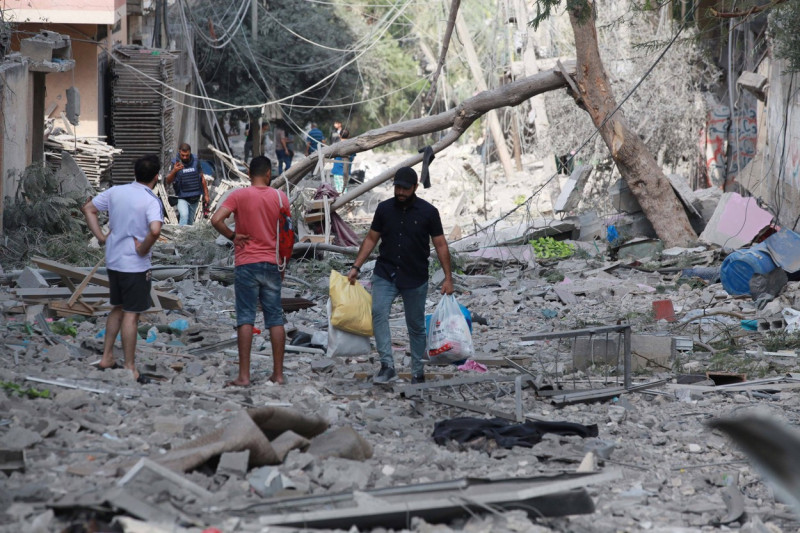 Palestinians walk through debris and destruction littering a street in al-Karama district in Gaza City