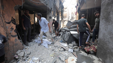 People are seen around destroyed buildings and debris at the Al-Shate'e refugee camp after an Israeli airstrike
