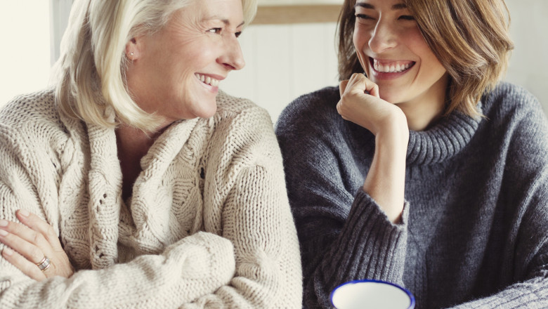 Laughing mother and daughter in sweaters drinking coffee