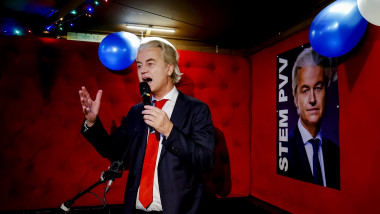 PVV leader Geert Wilders vorbeste la microfon, afis cu el in spate, pe fundal rosu si baloane