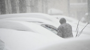 zăpadă pe mașini, un om își deszăpezește mașina