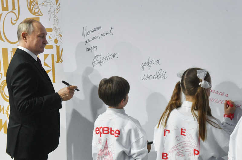 Putin scrie cu markerul pe o tablă alături de copii