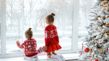 doua fetite imbracate in rosu se uita la ninsoare pe geam