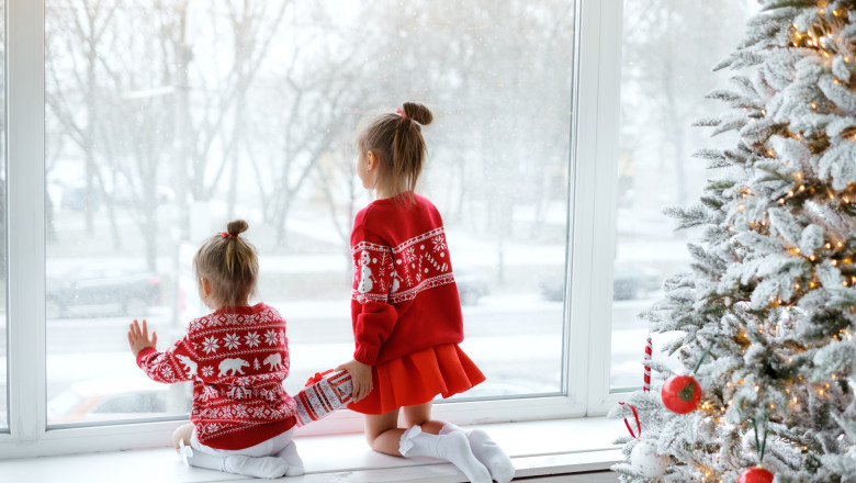 doua fetite imbracate in rosu se uita la ninsoare pe geam