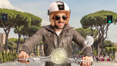 motociclist cu casca si ochelari de soare zambind pe scuter