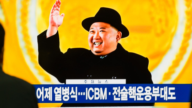 liderul nord-coreean Kim Jong Un cu pălărie pe cap salută mulțimea de la tribună