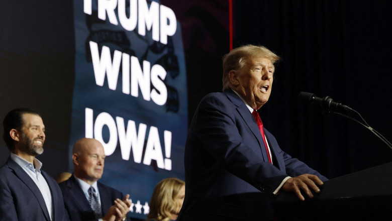 Donald Trump cu familia în spate și un ecran pe care e scris mesajul „Trump wins Iowa”