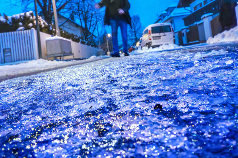 Eisregen morgens um 7:45 Uhr in München, Fußgänger geht vorsichtig auf der extrem glatten Straße, Januar 2024 Deutschlan