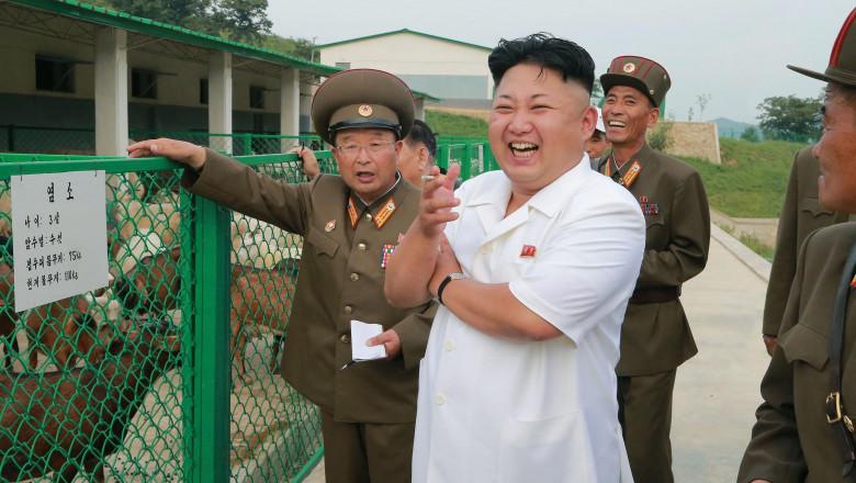 Kim Jong Un cu o țigară în mână râde alături de niște militari lângă un gard