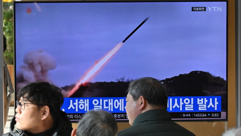 People watch a television screen showing a news broadcast with file footage of a North Korean missile test