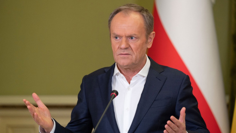 donald tusk la microfon, cu stegul poloniei in spate