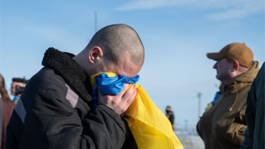 Un fost prizonier de război ucrainean plânge în timp ce strânge steagul Ucrainei, cu care își acoperă ochii