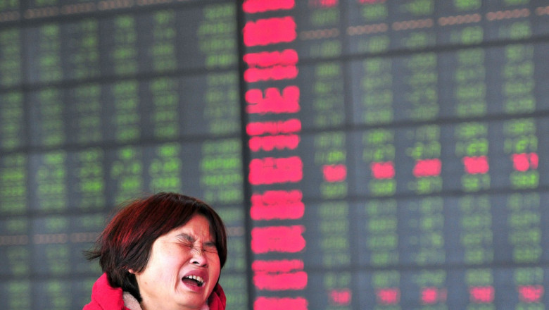 chinezoaică plânge în fața unui tabel cu cotații la bursă în roșu