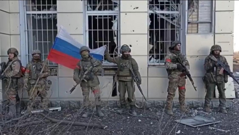 soldați ruși cu steaguri în fața unei clădiri cu geamuri sparte