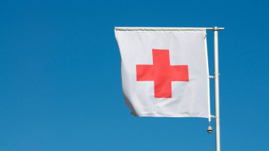 The flag of International Red Cross and Red Crescent Movement against a blue sky in Manno, Switzerland. The Red Cross is an international humanitarian