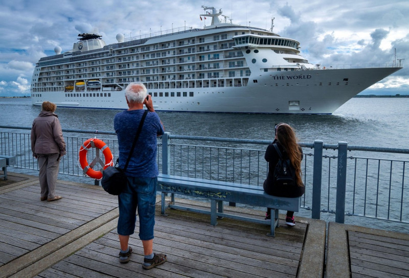 Wismar, Germany. 06th July, 2022. Passers-by watch from the pier as the luxury liner "The World" enters the seaport. On the 196-meter-long ship, more than 100 families from 20 nations live in their private apartments and travel around the world together.
