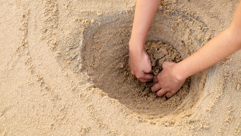 un copil sapa o groapa in nisip pe plaja