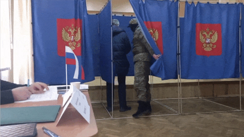 soldat inarmat in cabina de vot verifica cum voteaza alegetorul in rusia