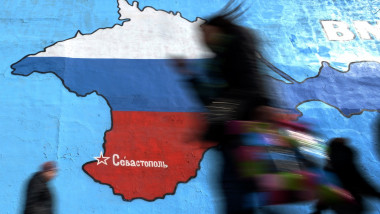 Pedestrians walk past an wall painting depicting a map of Crimean peninsula bearing the colours of Russia's national flag