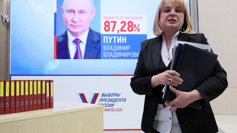 Femeie în fața unui ecran cu portretul lui Putin și scorul lui de la prezidențiale