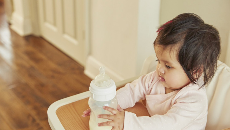 Baby girl holding baby milk bottle on high chair